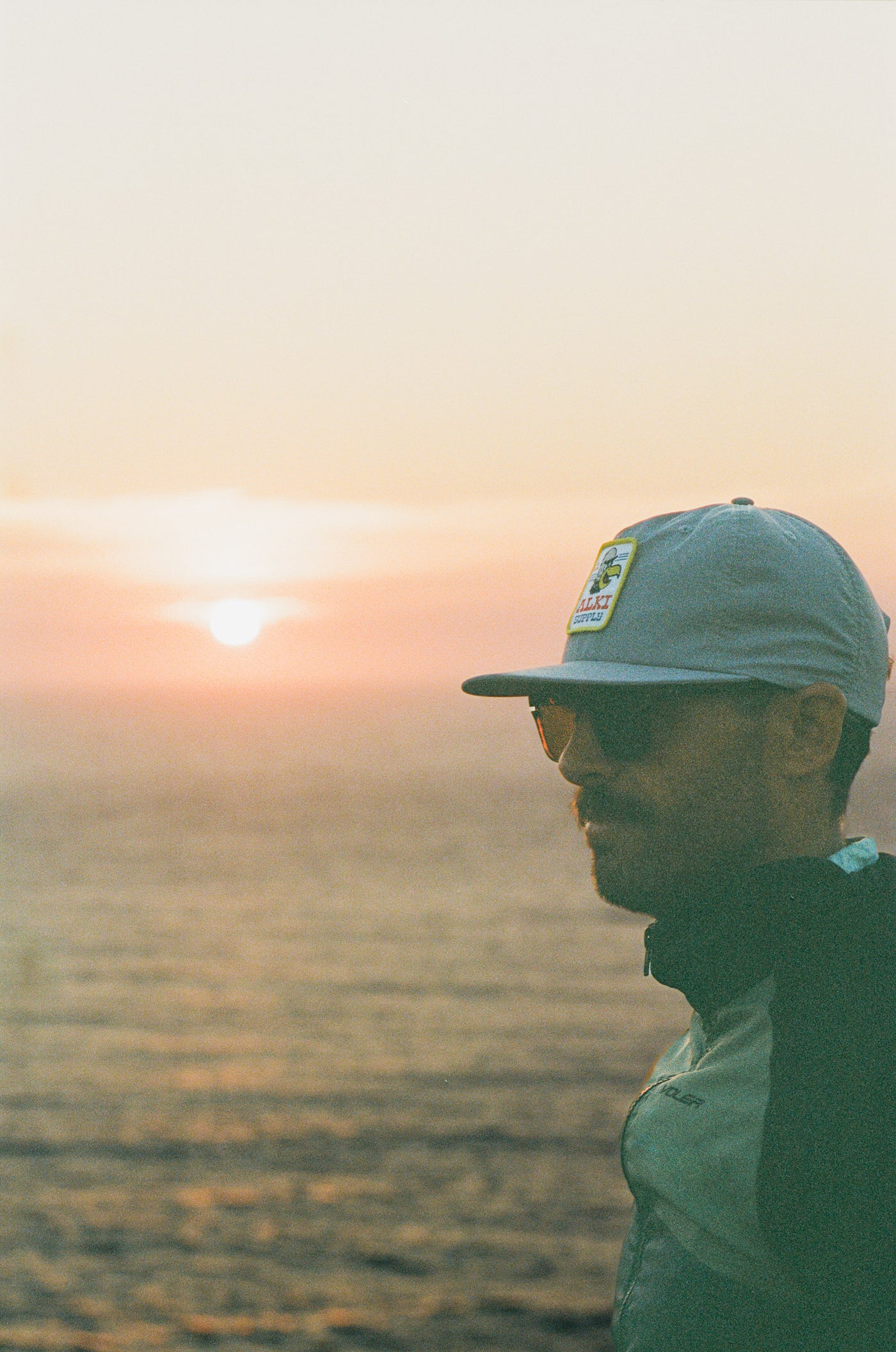 man wearing alki supply eagle eye hat with sunset background