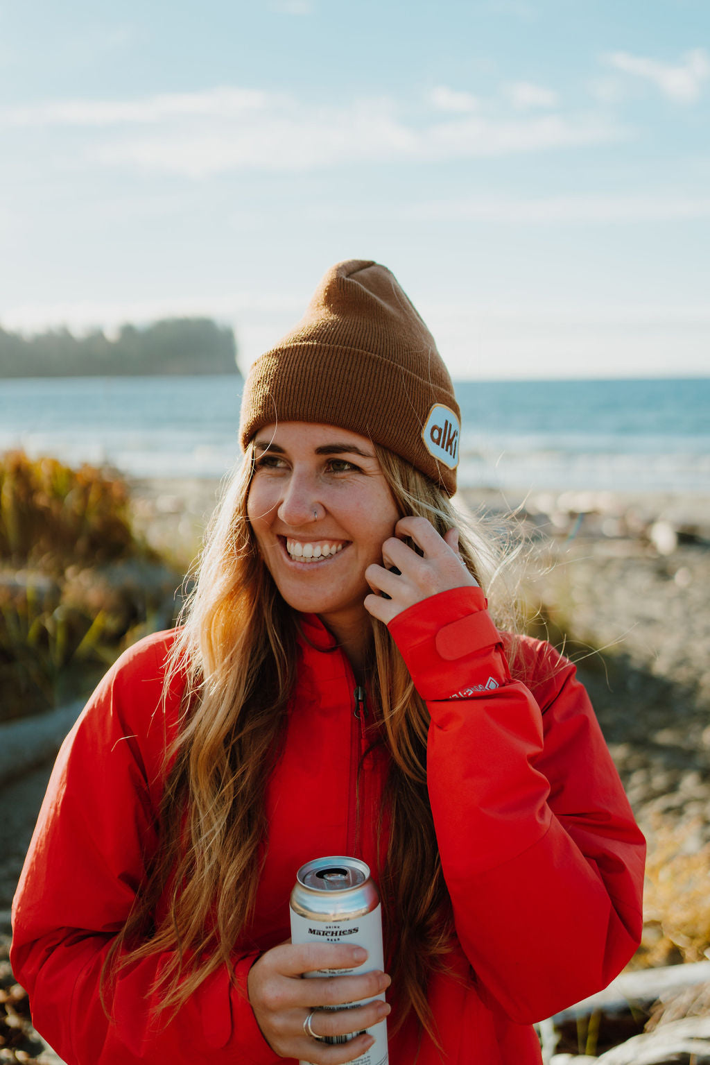 girl drinks a beer at the beach while wearing brown beanie with alki patch