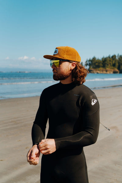 surfer in wetsuit wears brown snapback corduroy hat